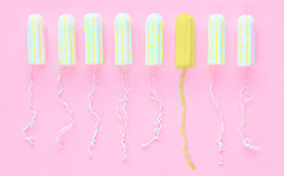 Eight tampons outside of their applicator sit in a row against a pink background and one is yellow.