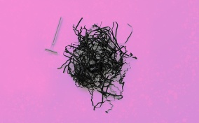 A pile of shredded black paper and a razor sit side by side on a pink background.