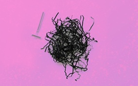 A pile of shredded black paper and a razor sit side by side on a pink background.