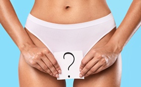 A woman in white panties holds a piece of paper that has a question mark drawn on it over her crotch. 