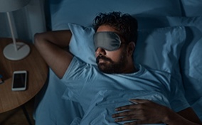 A man sleeps in bed with a facemask on.