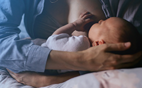 A mother breastfeeds her baby as it lays on a nursing pillow.