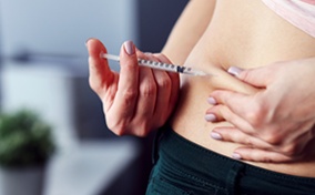 A woman pinches part of her stomach while administering an insulin injection.