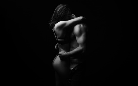 A couple stands and embraces each other intimately while under low light.