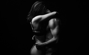 A couple stands and embraces each other intimately while under low light.