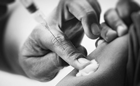 A finger holds a cotton ball to the spot on an arm of another person who has just received the meningitis vaccine.