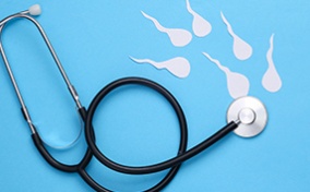 A stethoscope lays against a blue surface with white sperm swimming towards the chest piece.