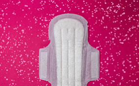 A maxipad with wings lays flat against a pink background with white dots.