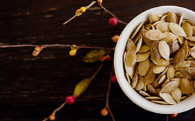 A small bowl of pumpkin seeds sits on top of a branch growing red and yellow berries.