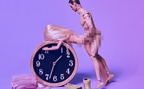 A Ken doll and a Barbie doll are in a sex position against an alarm clock with their pelvises pixelated.