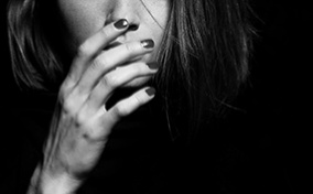 A woman with painted nails reaches her hand upward to cover her mouth.