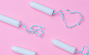 Four tampons without applicators lay against a pink surface.