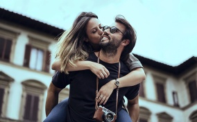 A man is giving a piggyback ride to a woman who is kissing his cheek.