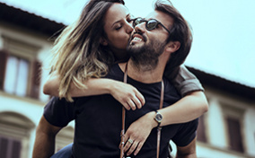 A man is giving a piggyback ride to a woman who is kissing his cheek.