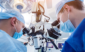 Two doctors look into a microsurgical machine during surgery.