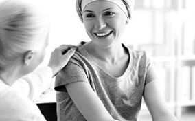 A woman with a headwrap smiles at another woman who touches her shoulder.