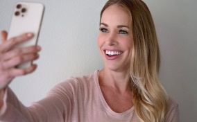 A woman smiles at her cellphone as she takes a selfie.
