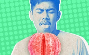 An oversized unpeeled grapefruit sits in front of a man with his tongue out to lick it.