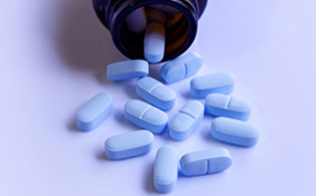 Blue pills spill out of a brown bottle onto a light blue surface.