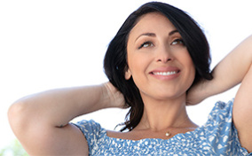 A woman leans back with her hands behind her head smiling.