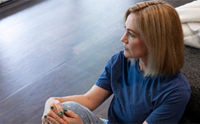 A woman sits on the wooden floor and looks into the distance.