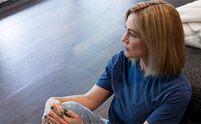 A woman sits on the wooden floor and looks into the distance.