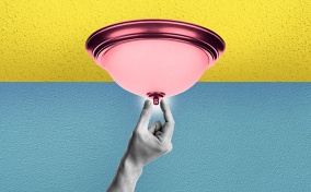 A black and white hand reaches up to pinch the tip of a pink light fixture that is on a yellow ceiling in front of a blue background.