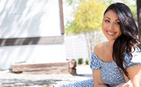 A woman in a blue dress sits outside and smiles at the camera.