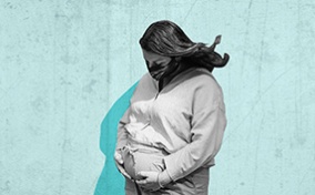 A pregnant person wears a medical mask and holds their pregnant belly with a blue background behind them.