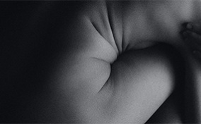 A naked person crouches down and wraps their arms around their knees.