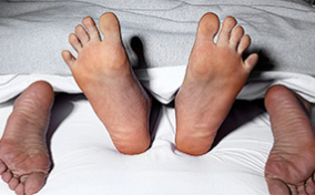 Two pairs of feet peek out from under white sheets in bed.