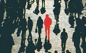 A red figure is in the center of a dark crowd walking on the road.
