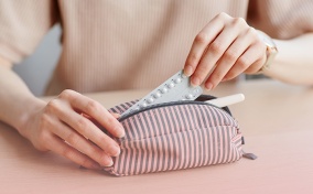 A woman pulls her packet of birth control pills from a pouch as it sits on a table.