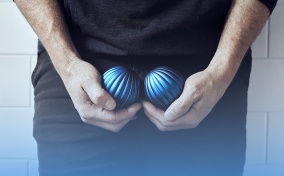 A man holds one blue ball in each hand cupped down near his groin. 