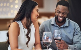 A man and woman are smiling as they talk and drink wine on a date.