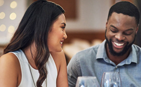 A man and woman are smiling as they talk and drink wine on a date.