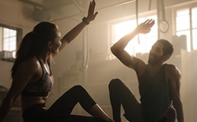 A man and a woman high-five while sitting down after a workout.