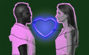 A couple stand across from each other with a neon heart light heart between them.