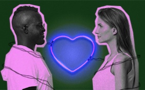 A couple stand across from each other with a neon heart light heart between them.