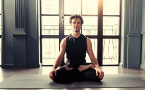 A man sits cross legged on a yoga mat with his eyes closed in meditation.