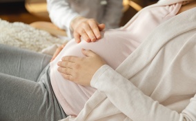 A pregnant woman holds her belly in two places while another person presses on it from the top.