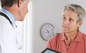A male patient sits in front of a doctor with a tablet during a health screening.