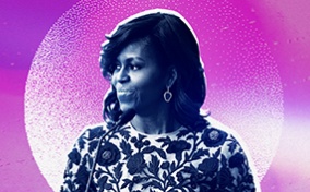 Michelle Obama stands in front of a microphone looking to her right with a fuchsia and white background.