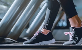 A person is walking on a treadmill with only their lower legs and feet showing.