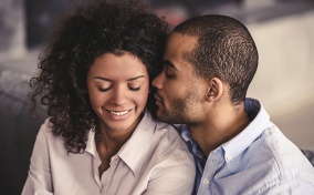 A woman closes her eyes and smiles while her partner puts his face close to her ear.