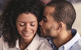 A woman closes her eyes and smiles while her partner puts his face close to her ear.