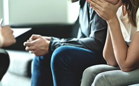 A woman sits next to a man on a couch with her hand in her hands.