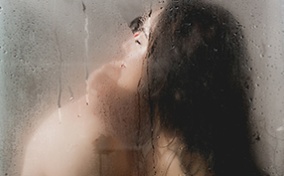 A couple embraces inside of a steamy shower.