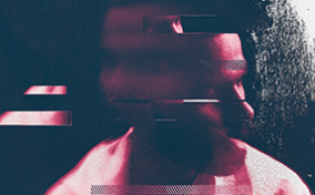 A man lit in red looks to the left while part of his face looks to the right against a black and white background.