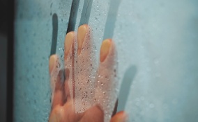 A hand streaks down a fogged up window covered in condensation.